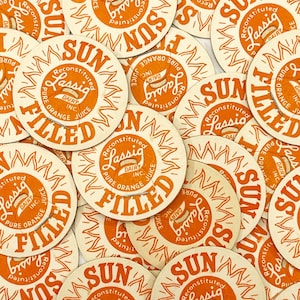 Puede incluir: Primer plano de una pila de tapas redondas de botellas de leche, de color naranja y blanco, con el texto "SUN FILLED" y "Reconstituted Lassig Dairy Inc. Pure Orange Juice" impreso en ellas.