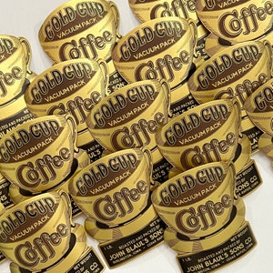 Puede incluir: Una colección de etiquetas de café vintage doradas con el texto "Gold Cup Vacuum Pack Coffee" impreso en cada etiqueta. Las etiquetas presentan una ilustración estilizada de una taza de café.