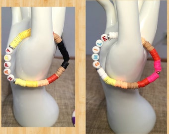 May include: Two colorful beaded bracelets with the words "HAPPY" and "SMILE" spelled out in white letters. The bracelets are made with small, round beads in various colors, including yellow, orange, red, pink, blue, and black.