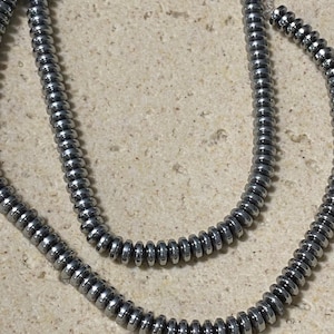 May include: Two strands of metallic silver-coloured disc-shaped beads strung on clear filament. The beads have a smooth, reflective surface and a uniform, flattened circular shape, arranged in a continuous line along the thin, transparent cord.