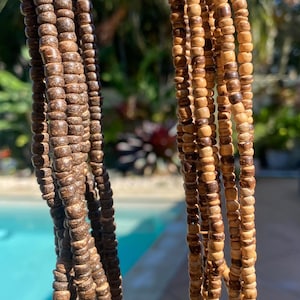 May include: Two multi-strand necklaces made of small, cylindrical wooden beads. The left necklace features dark brown, textured beads, while the right necklace consists of lighter, tan-coloured wooden beads. Both are arranged in vertical strands.