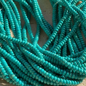 May include: A large collection of small, round, turquoise-coloured beads strung together on multiple thin threads. The beads have a smooth, uniform finish and a vibrant, consistent teal hue, creating a dense, textured cluster of jewellery components.