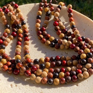 May include: A collection of spherical wooden beads arranged in multiple strands. The beads feature a variety of natural wood tones, including light tan, deep red, dark brown, and black, each displaying distinct wood grain patterns and textures.