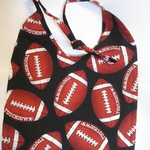 Könnte beinhalten: Eine schwarze Tragetasche mit einem sich wiederholenden Muster aus roten und weißen American-Football-Bällen. Die Worte "TOUCHDOWN!" sind auf den Fußbällen aufgedruckt. Die Tasche hat einen Schulterriemen und ist aus Stoff.