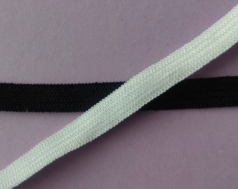 May include: Two pieces of elastic, one black and one white, are lying on a purple surface. The elastic is a common material used for sewing and crafting.
