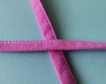 May include: Close-up of a pink fabric strap with white stitching. The strap is folded over itself and the edges are visible.