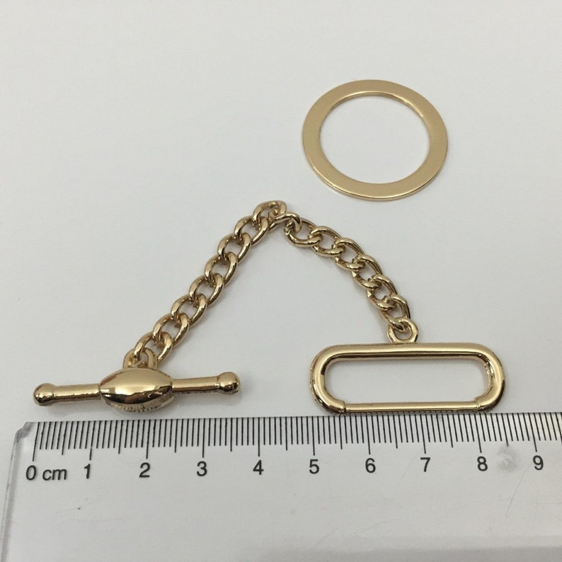 Puede incluir: Una cadena dorada con un anillo, un cierre de palanca y un bucle rectangular. La cadena mide aproximadamente 8 cm de largo.