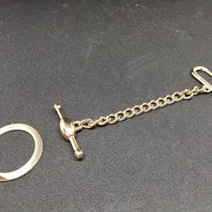 Puede incluir: Una cadena dorada con un anillo redondo y dos cierres. La cadena est&aacute; hecha de metal y tiene un dise&ntilde;o cl&aacute;sico.