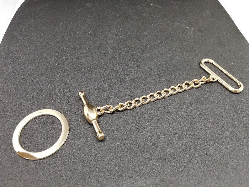 Puede incluir: Una cadena dorada con un anillo redondo y dos cierres. La cadena est&aacute; hecha de metal y tiene un dise&ntilde;o cl&aacute;sico.