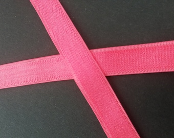 May include: Two pieces of pink elastic ribbon are crossed over each other on a black background.