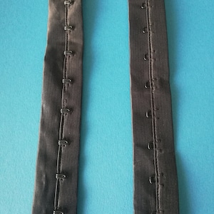 May include: Two black elastic straps with rows of metal hooks and eyes for adjusting the length of a garment.