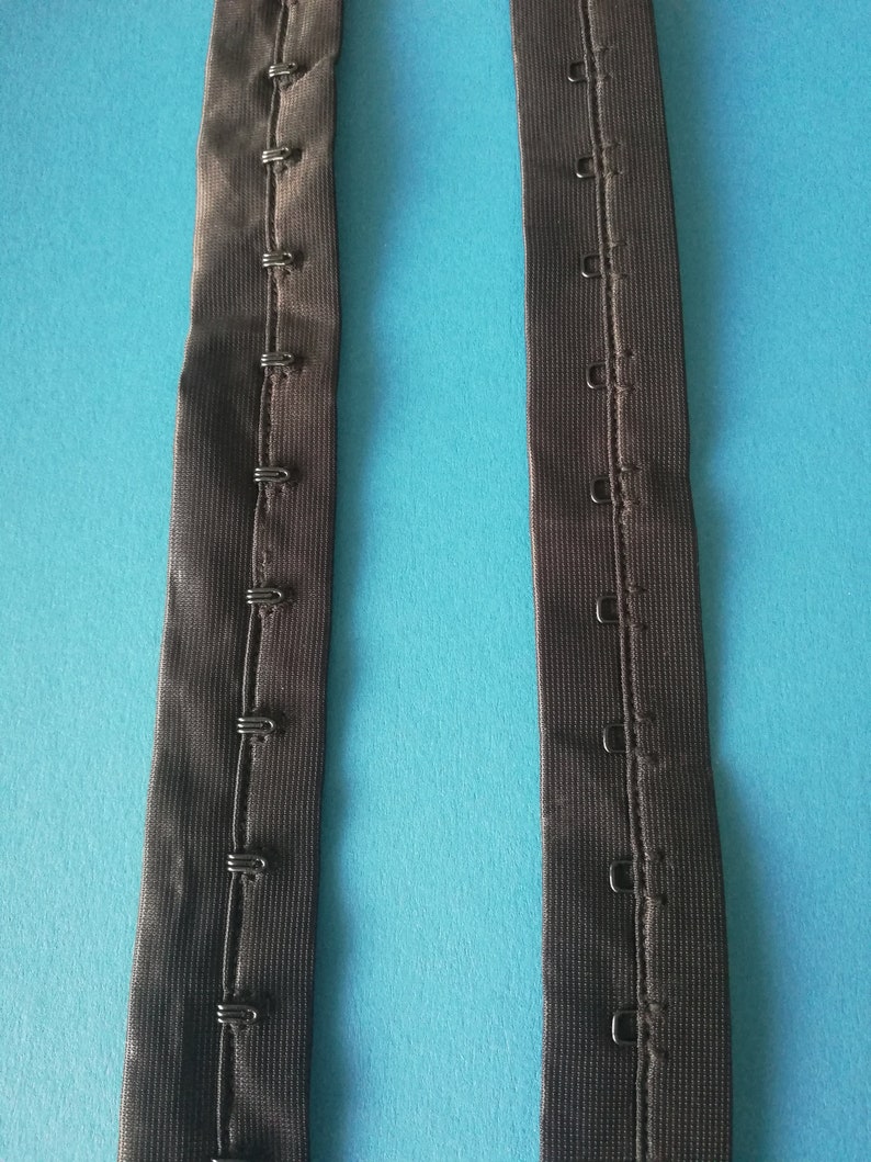 May include: Two black elastic straps with rows of metal hooks and eyes for adjusting the length of a garment.