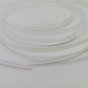 May include: A close-up of a white, flexible, and translucent plastic trim. The trim is coiled and appears to be about 1/4 inch wide.