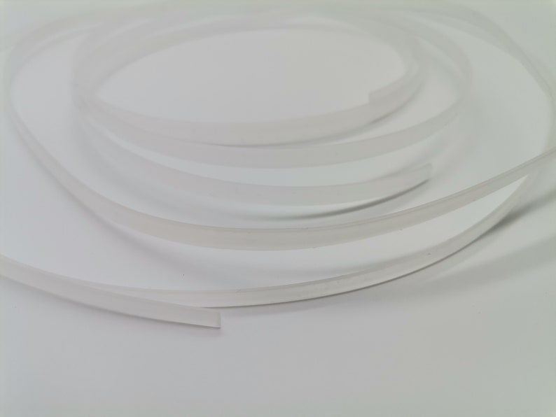 May include: A close-up of a white, flexible, and translucent plastic trim. The trim is coiled and appears to be about 1/4 inch wide.