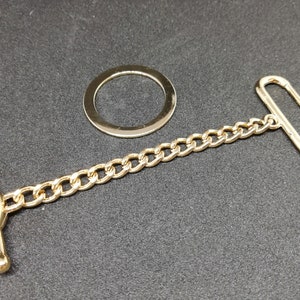 Puede incluir: Una cadena dorada con un anillo redondo, un cierre de palanca y un anillo en D. La cadena mide aproximadamente 30 cm de largo.