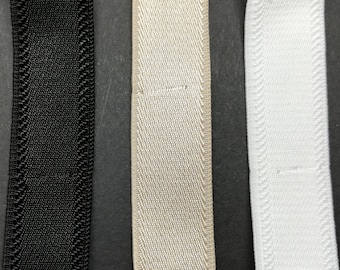 May include: Three strips of flat elastic webbing arranged vertically. The left strip is black, the centre strip is beige, and the right strip is white. Each strip features a woven texture with reinforced edges and a consistent width throughout.