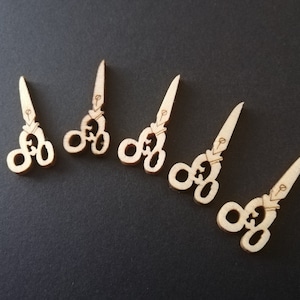 Può includere: Cinque forme di forbici ritagliate in legno. Le forbici sono tutte della stessa dimensione e forma, e sono tutte rivolte nella stessa direzione. Le forbici sono di colore marrone chiaro.