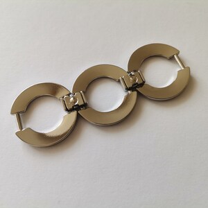 May include: Three silver metal rings connected together, forming a chain. Each ring has a smooth, rounded surface and a small, circular opening in the center.