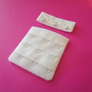 Op de afbeelding: Witte bh-verlenger met drie rijen haken en ogen. De verlenger is gemaakt van een zachte, witte stof en heeft een gladde afwerking.