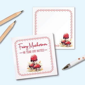 May include: Two square note pads with a red vine border and a watercolour illustration of three red mushrooms at the bottom. The top pad features the text Fairy Mushroom and 48 TEAR OFF NOTES in red. Two wooden pencils and a white pen are included.