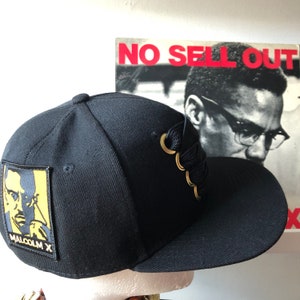 Malcolm X - Specialdesignad svart snapback-keps med tjock spets och guldfärgad Malcolm X-lapp.