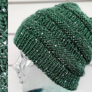 May include: A dark green knit beanie with silver sequins. The hat is made of a thick, textured yarn and has a ribbed brim. The sequins are scattered throughout the knit, adding a touch of sparkle. The beanie is a winter accessory.