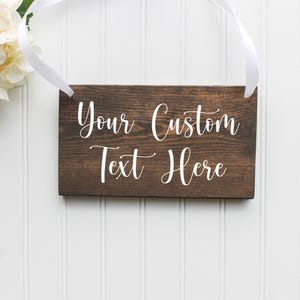 May include: A rustic wooden sign with white text that reads "Your Custom Text Here". The sign is hanging from a white ribbon.