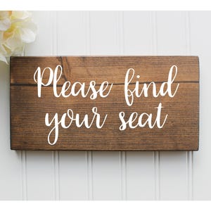 May include: A rustic wooden sign with the text "Please find your seat" in white lettering.