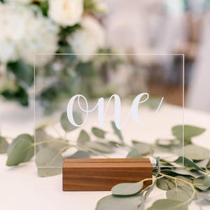 Clear acrylic table number sign with black lettering and walnut wood stand on white background for listing display