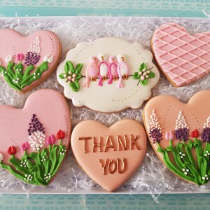 May include: A gift box filled with six pink heart-shaped cookies decorated with floral designs and the words "Thank You".
