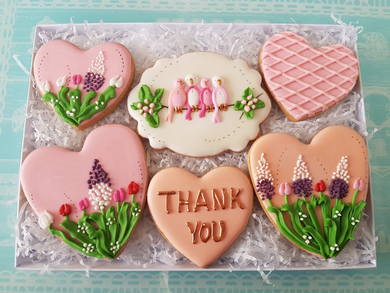 May include: A gift box filled with six pink heart-shaped cookies decorated with floral designs and the words "Thank You".