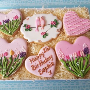 May include: A gift box filled with six pink heart-shaped cookies decorated with flowers, birds, and the text "Happy 21st Birthday Sophie".
