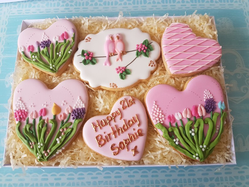 May include: A gift box filled with six pink heart-shaped cookies decorated with flowers, birds, and the text "Happy 21st Birthday Sophie".