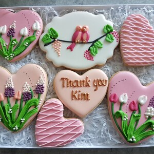 May include: A set of six pink heart-shaped cookies decorated with flowers, birds, and the text "Thank you Kim".