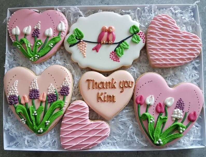 May include: A set of six pink heart-shaped cookies decorated with flowers, birds, and the text "Thank you Kim".