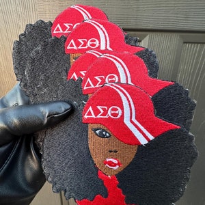 May include: Five red and white embroidered patches featuring a black woman with an afro hairstyle wearing a red and white baseball cap with the letters "ΔΣΘ" on the front.
