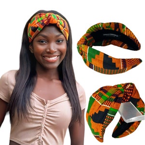May include: A woman wearing a patterned knotted headband in shades of orange, green, and black. The headband is made of fabric and has a wide band. The text "EQUALLY ROOTED" is visible on the inside of the headband.