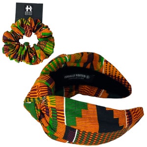 May include: A patterned headband and scrunchie set in orange, green, and purple. The headband has a knotted design, and the scrunchie is circular. The brand name "Equally Rooted" is visible on a tag and the headband. The fabric has an African print.