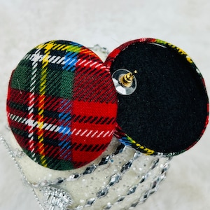 May include: A pair of round, red, green, yellow, and white plaid fabric earrings with black felt backing and gold posts.