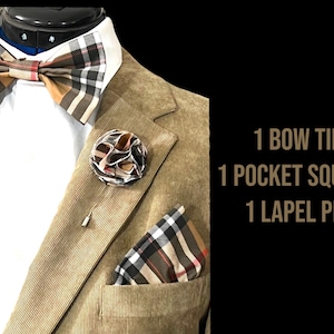 May include: A brown plaid bow tie, pocket square, and lapel pin. The bow tie and pocket square have a brown, black, and white plaid pattern. The lapel pin is a brown, black, and white flower.