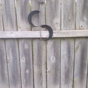 May include: A metal sculpture with a geometric design and a green stone at the top. The sculpture is attached to a long metal rod that is anchored into the ground.