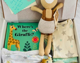 May include: A baby gift box containing a giraffe plush toy, a book titled "Where's the Giraffe?", a star-patterned blanket, a Gerber onesie, and a giraffe teether. The box also includes a greeting card with handwritten text.