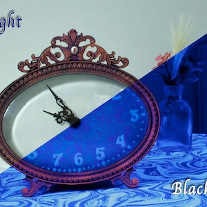 Puede incluir: Un reloj ovalado con agujas negras y números romanos. El reloj está sobre una mesa con un patrón de mármol azul y blanco. La esfera del reloj es blanca en el lado izquierdo de la imagen y azul en el lado derecho de la imagen. Las palabras "Daylight" y "Blacklight" están escritas encima del reloj.