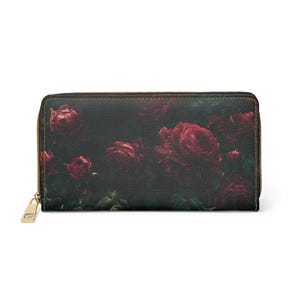 Può includere: Un portafoglio nero con cerniera dorata e un motivo floreale di rose. Le rose sono di un rosso intenso, su uno sfondo scuro. Il portafoglio è rettangolare e sembra essere in pelle.