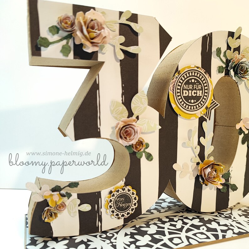May include: A 3D number 30 made of cardboard with black and white stripes. The number is decorated with paper flowers, leaves, and a small circle with the text "Nur f&uuml;r Dich".