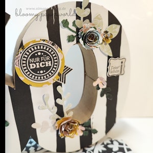 May include: A white and black striped paper craft number with a brown paper center. The number is decorated with paper flowers, leaves, and a round sticker that says "Nur f&uuml;r Dich".