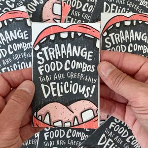 May include: A person holding several stickers. Each sticker has a black background with white text that reads "STRAAANGE FOOD COMBOS THAT ARE CREEPISHLY DELICIOUS!". The stickers feature an illustration of a mouth.