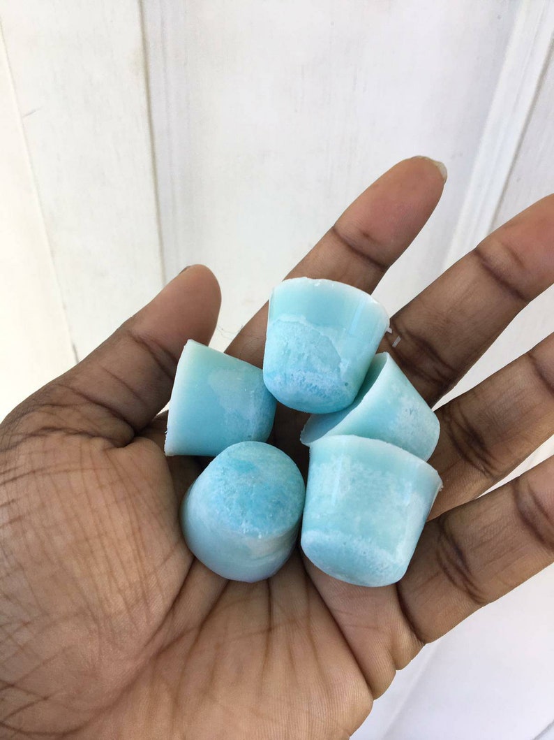 Puede incluir: Una mano sosteniendo un grupo de seis peque&ntilde;as y redondas ceras de fusi&oacute;n de color azul claro.