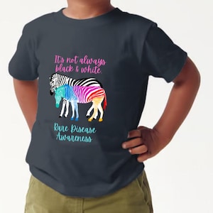 Puede incluir: Una camiseta azul oscuro con un diseño de cebra colorido y el texto "No siempre es blanco y negro. Concientización sobre enfermedades raras."