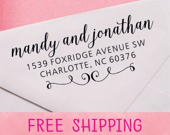 May include: A white envelope with a black return address stamp that reads "mandy and jonathan 1539 Foxridge Avenue SW Charlotte, NC 60376". The stamp has a decorative flourish at the bottom. The envelope has the words "FREE SHIPPING" printed in pink at the bottom.